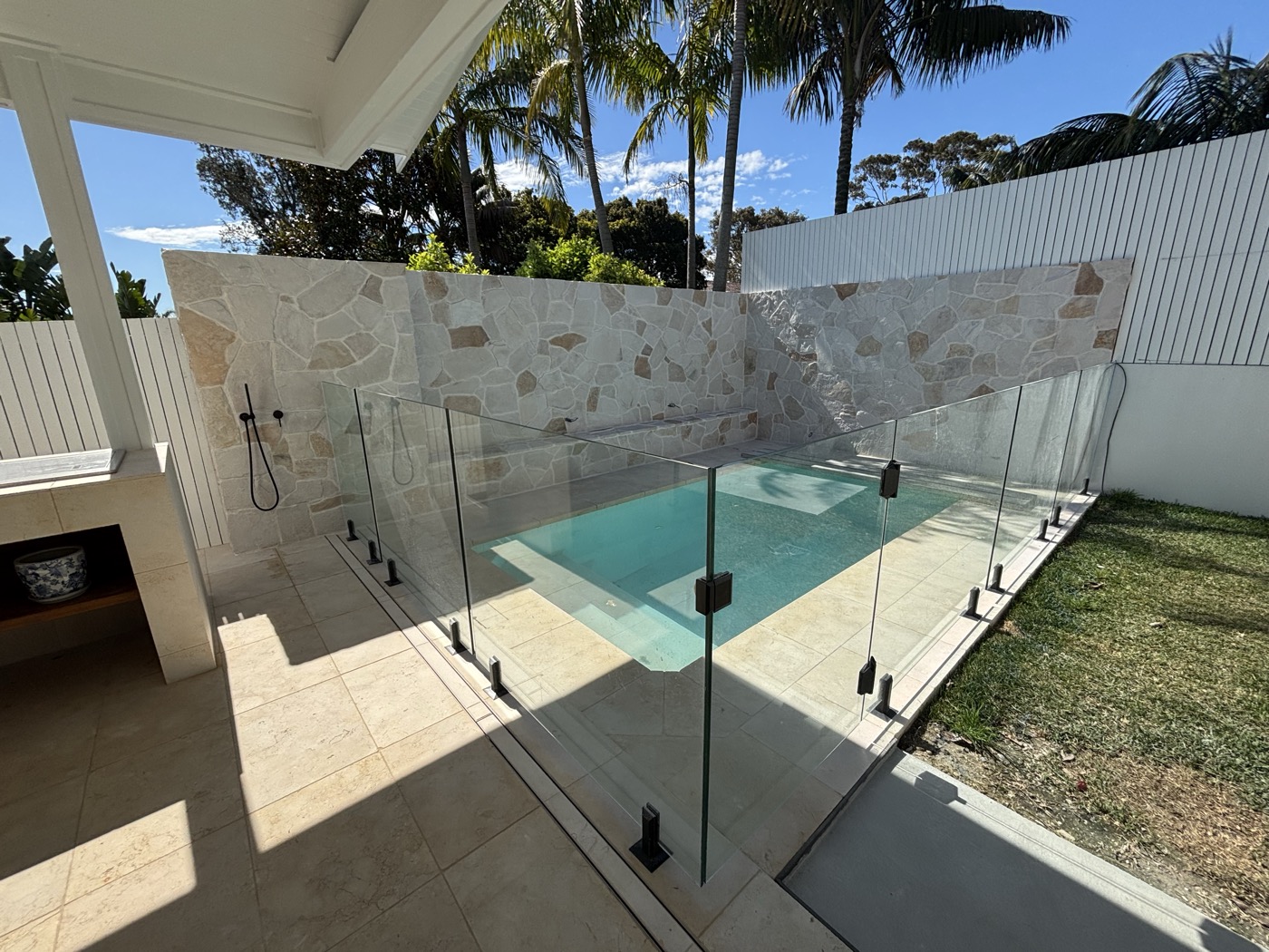 Pool surrounded by natural stone feature wall and glass fencing